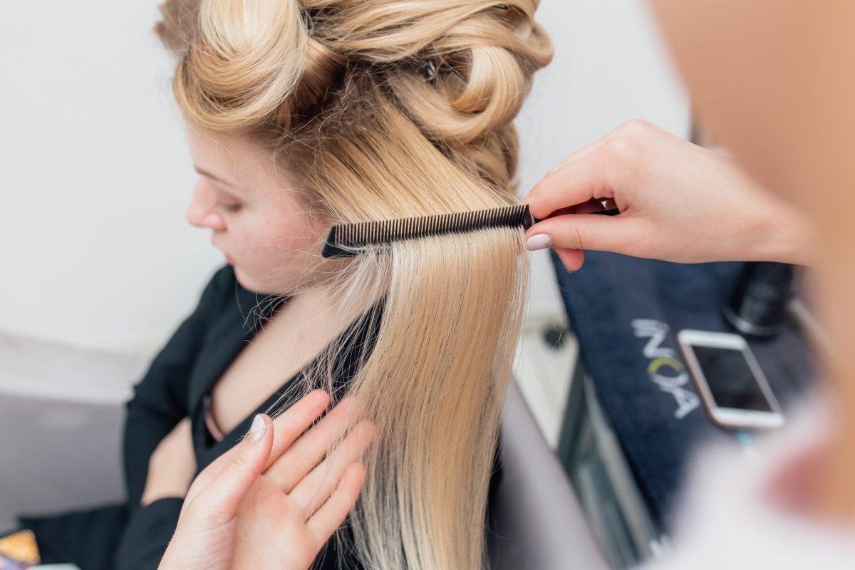 Hairdressers hands drying long blond hair with blow dryer and round brush