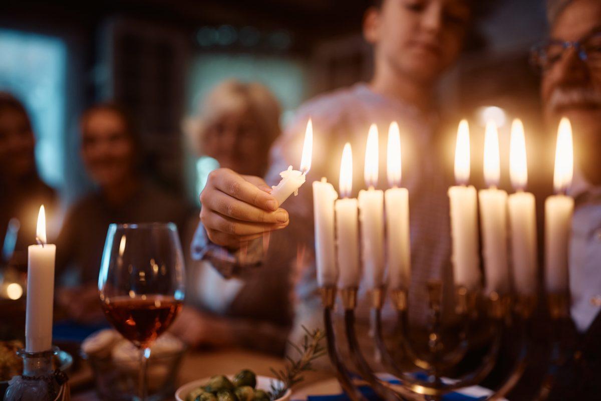 Close up of boy lighting candles in menorah while celebrating Hanukkah with his family at dining table.
