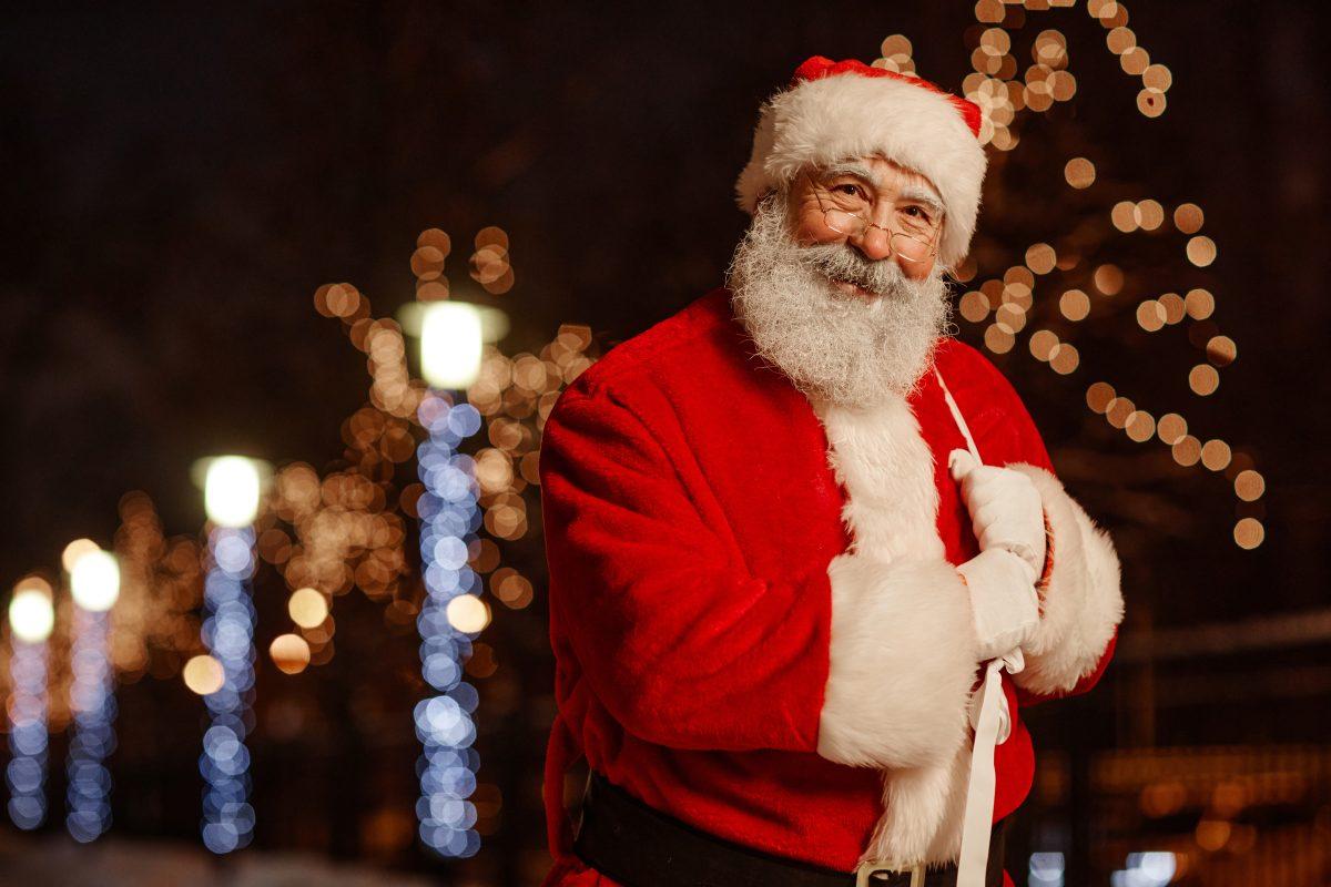 Portrait of joyful Santa Claus standing outdoors in street decorated with garland lightsp